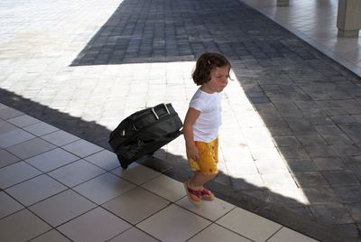 High angle view of girl with luggage walking on footpath