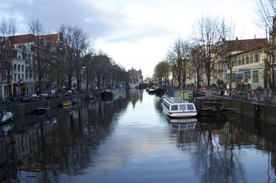 Boats moored on canal in city against sky