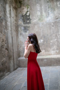 Side view of woman praying while standing against wall