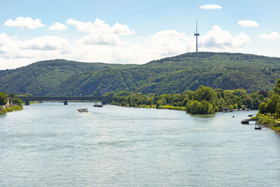 A beautiful view of the river rhine in west germany on which ships, dense forest, bridge, and tower.
