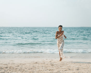 Full length of woman running on shore at beach against sky
