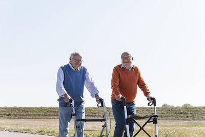Two old friends walking on a country road, using wheeled walkers