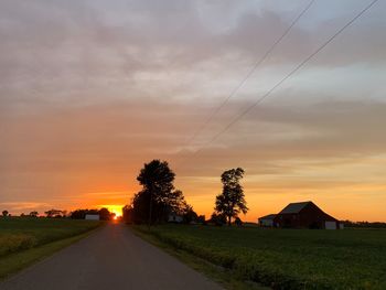 Road amidst field against sky during sunset