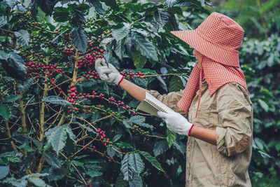 Midsection of woman holding plants against trees