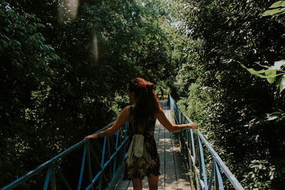 Rear view of woman standing on footbridge in forest