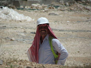 Smiling man wearing keffiyeh and hardhat standing on field