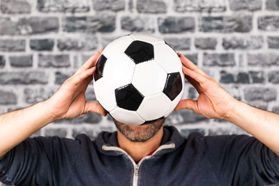 Close-up of man holding soccer ball against wall