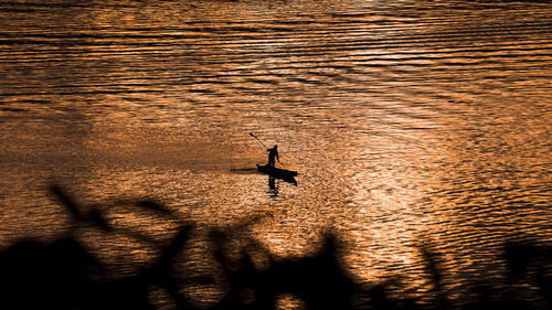 Silhouette person on sea against sky during sunset