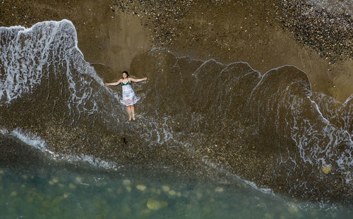 Woman with white dress resting on a sandy beach with braking waves on the shore. overhead shot. 