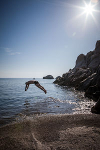 Shirtless man diving into sea against sky