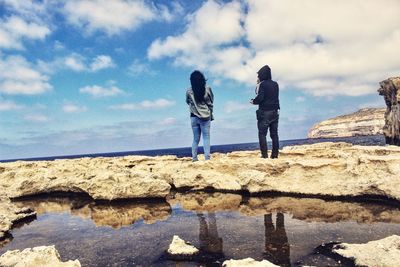 Rear view of friends standing on rock formation against sky