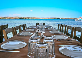 Empty chairs and tables at restaurant by sea against sky