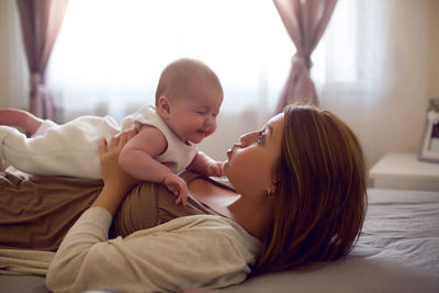 Young mother with red hair is lying on the bed with her daughter at home in the morning