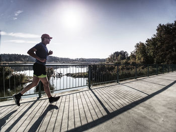Side view silhouette of a runner man running on the beach bridge at sunset with sun in background