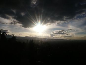 Sunlight streaming through clouds over silhouette landscape