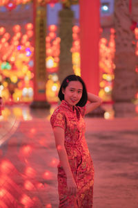Portrait of woman standing against illuminated red lights at night