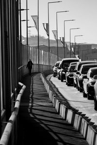 Cars on street against sky in city with a woman walking alone.