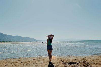 Rear view of woman standing on shore against clear sky