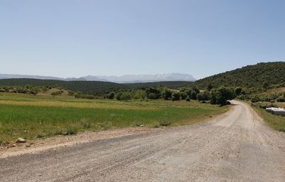 Road leading towards mountains against clear sky