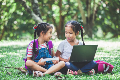 Schoolgirls talking while using laptop while sitting in park
