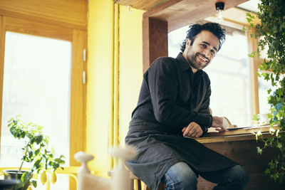 Portrait of happy waiter sitting on stool