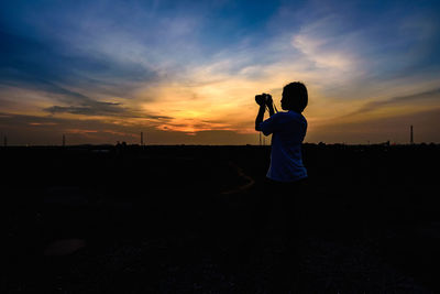 Young woman photographing against sky during sunset