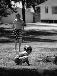 Water spraying on shirtless boy with sister in yard