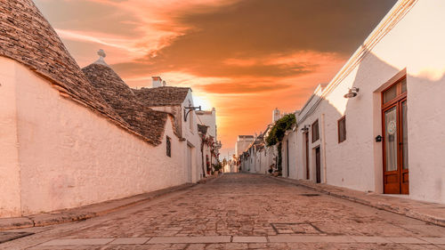 Street amidst buildings against sky during sunset