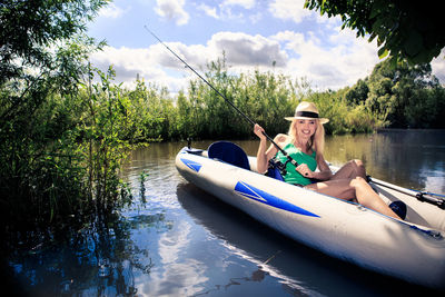 Mid adult woman holding fishing net while canoeing on lake against cloudy sky