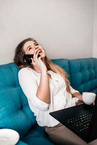Young woman using mobile phone while sitting on sofa at home