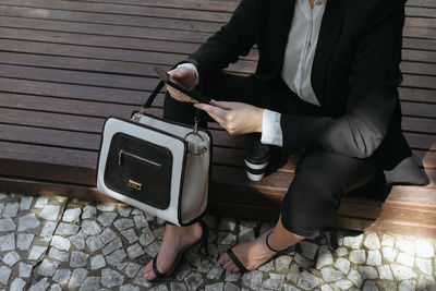 Low section of businesswoman using mobile phone while holding bag outdoors