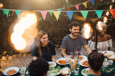 Happy multi-ethnic friends enjoying dinner at table during garden party
