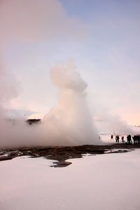 People near geyser against sky