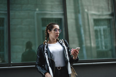 Beautiful young woman using phone standing against building in city