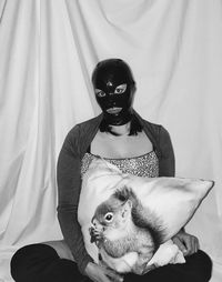 Portrait of woman wearing latex mask while sitting with pillow at home