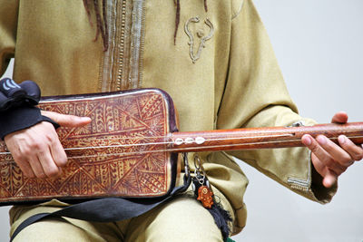 Midsection of man playing string instrument against wall