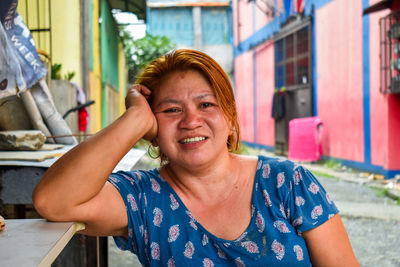 Portrait of mature woman smiling while sitting against houses