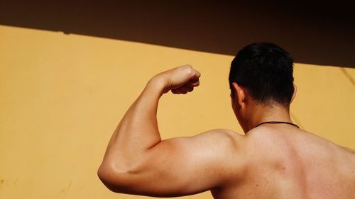 Rear view of shirtless man standing against yellow wall