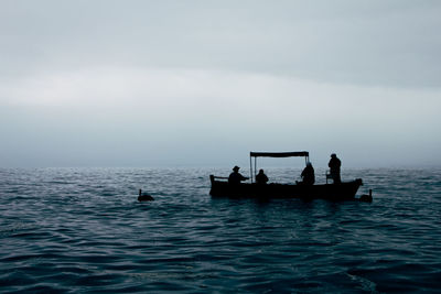 Silhouette people in boat sailing on sea against sky