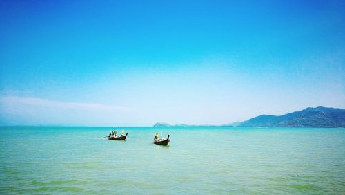 Boats in sea against clear blue sky