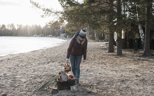 Woman putting a kettle on an outdoor fire at the beach in winter