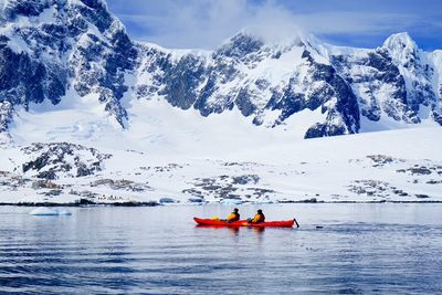 Men boating in lake by snowcapped mountains