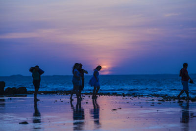 People walking at beach against sky during sunset