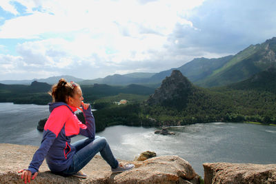 Side view of woman sitting on mountain against cloudy sky