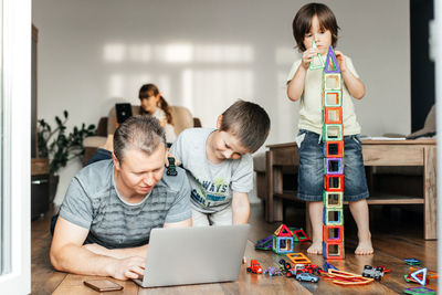 Parent, dad trying to work at home on a laptop. children play nearby. be a working parent.