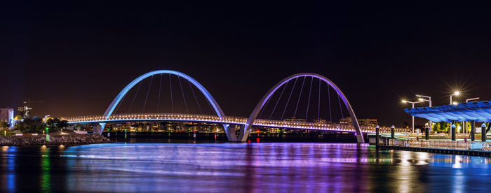 Illuminated bridge over water against clear sky at night