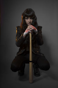 Portrait of young female model crouching with baseball bat against gray background