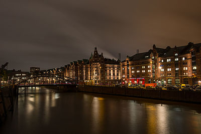 Illuminated buildings by river against sky in city at night