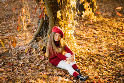 Child girl is sitting near a tree in an autumn city park, a child is playing and enjoying an autumn