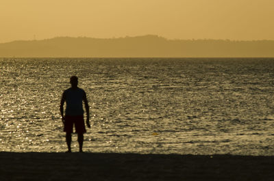 Rear view of silhouette man standing at beach during sunset